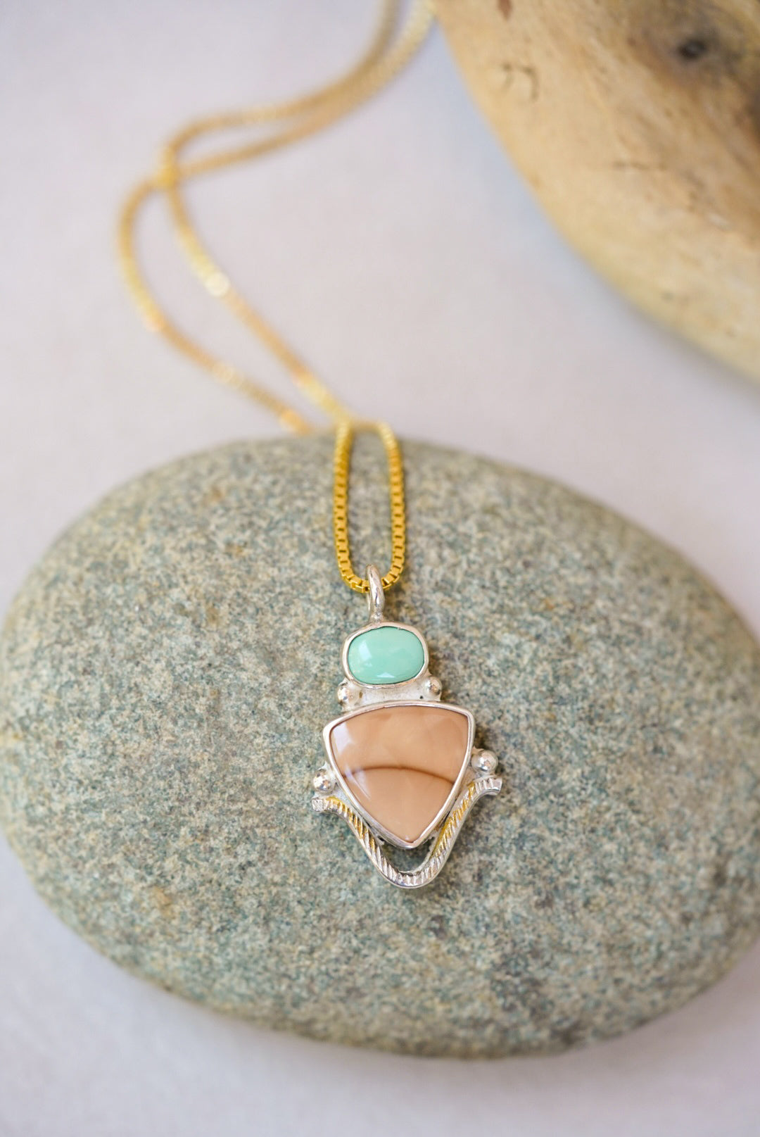 Necklace with a pendant featuring a turquoise stone and pinkish-beige center on a stone surface.