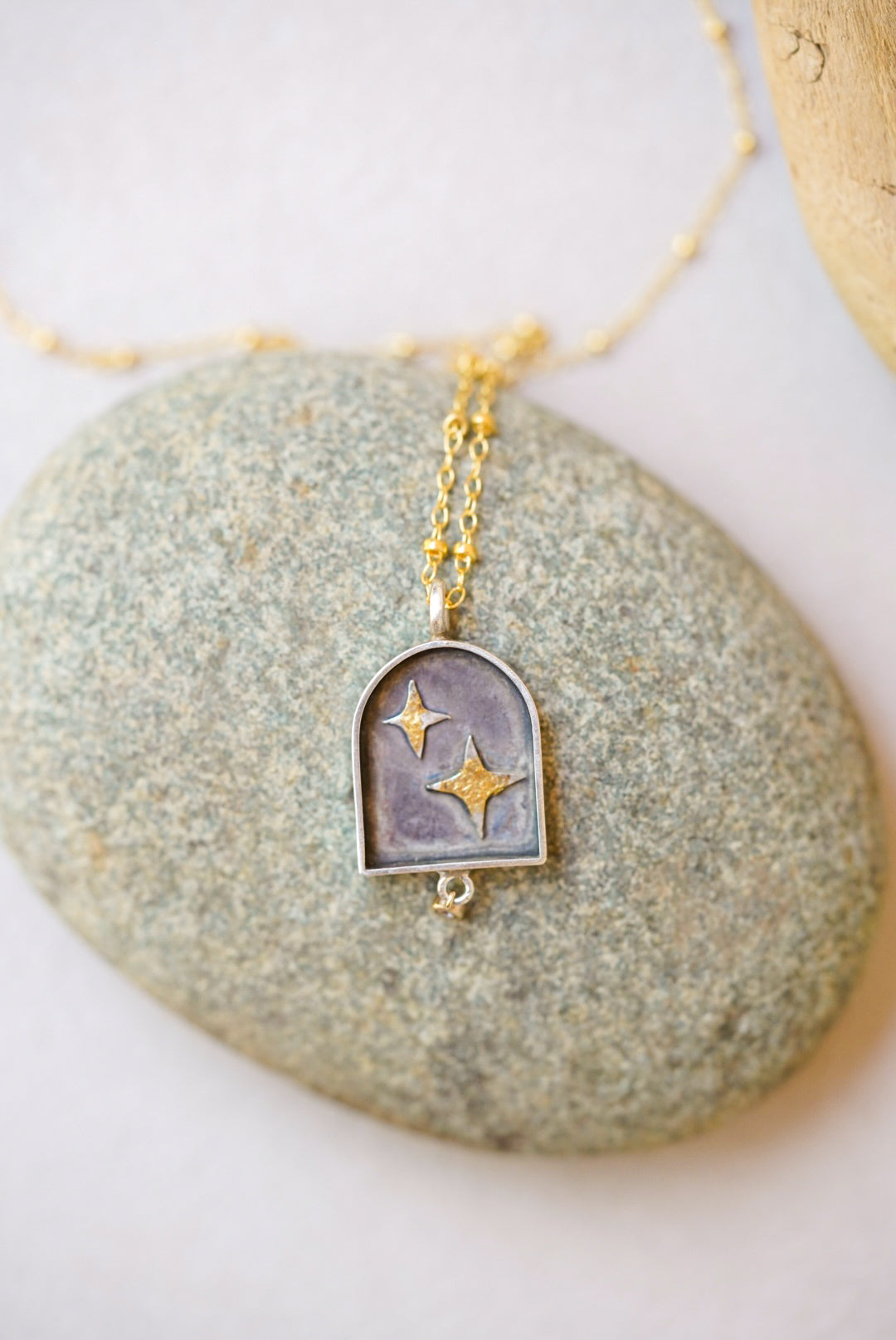 pendant with celestial design and a small diamond dangle on a river rock