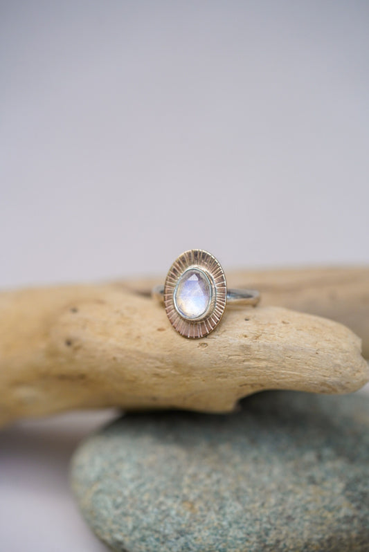 Moonstone ring on top of a piece of driftwood with a white background