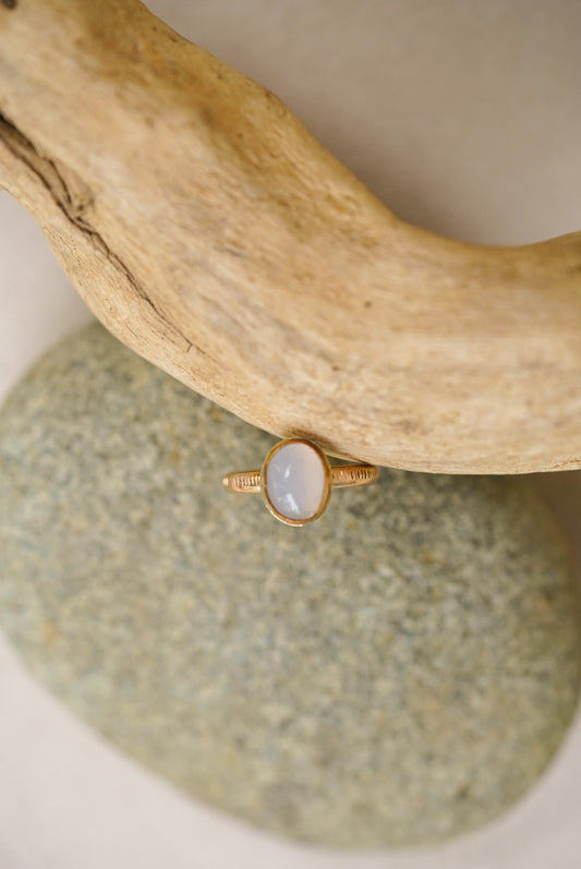 Light purple chalcedony stone with gold ring on a rock next to driftwood