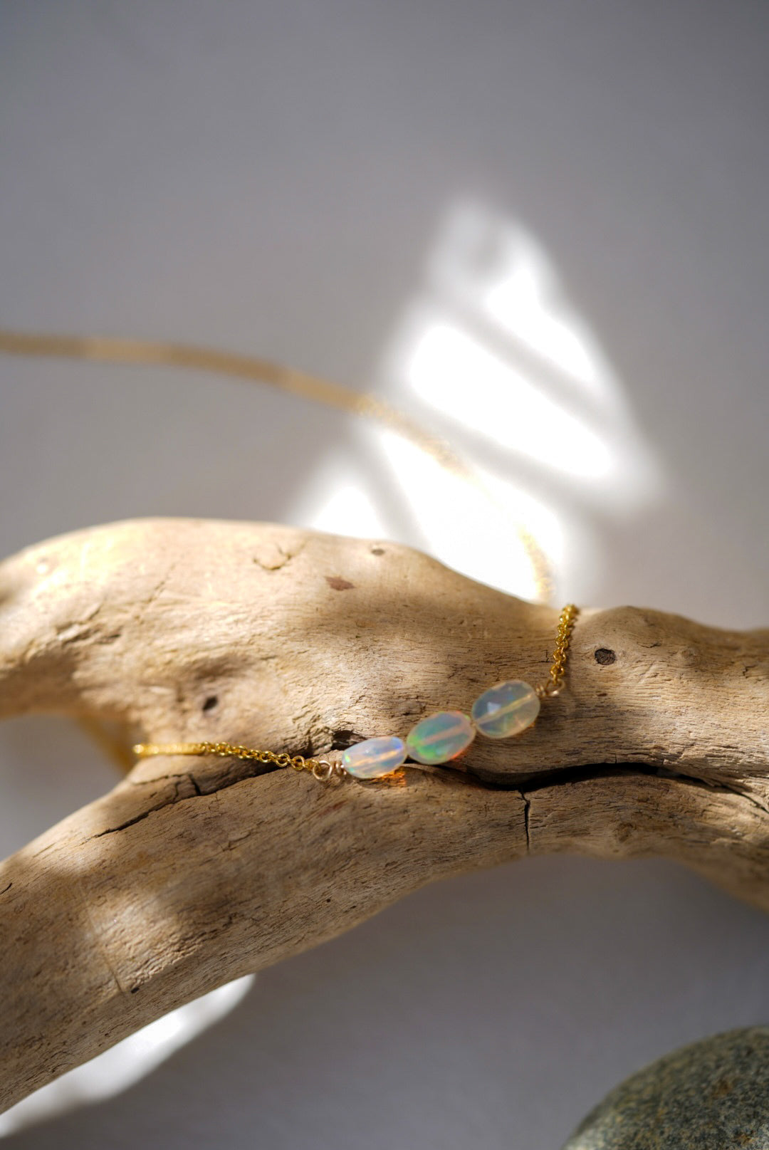 Opal necklace on a piece of driftwood with sunlight casting shadows