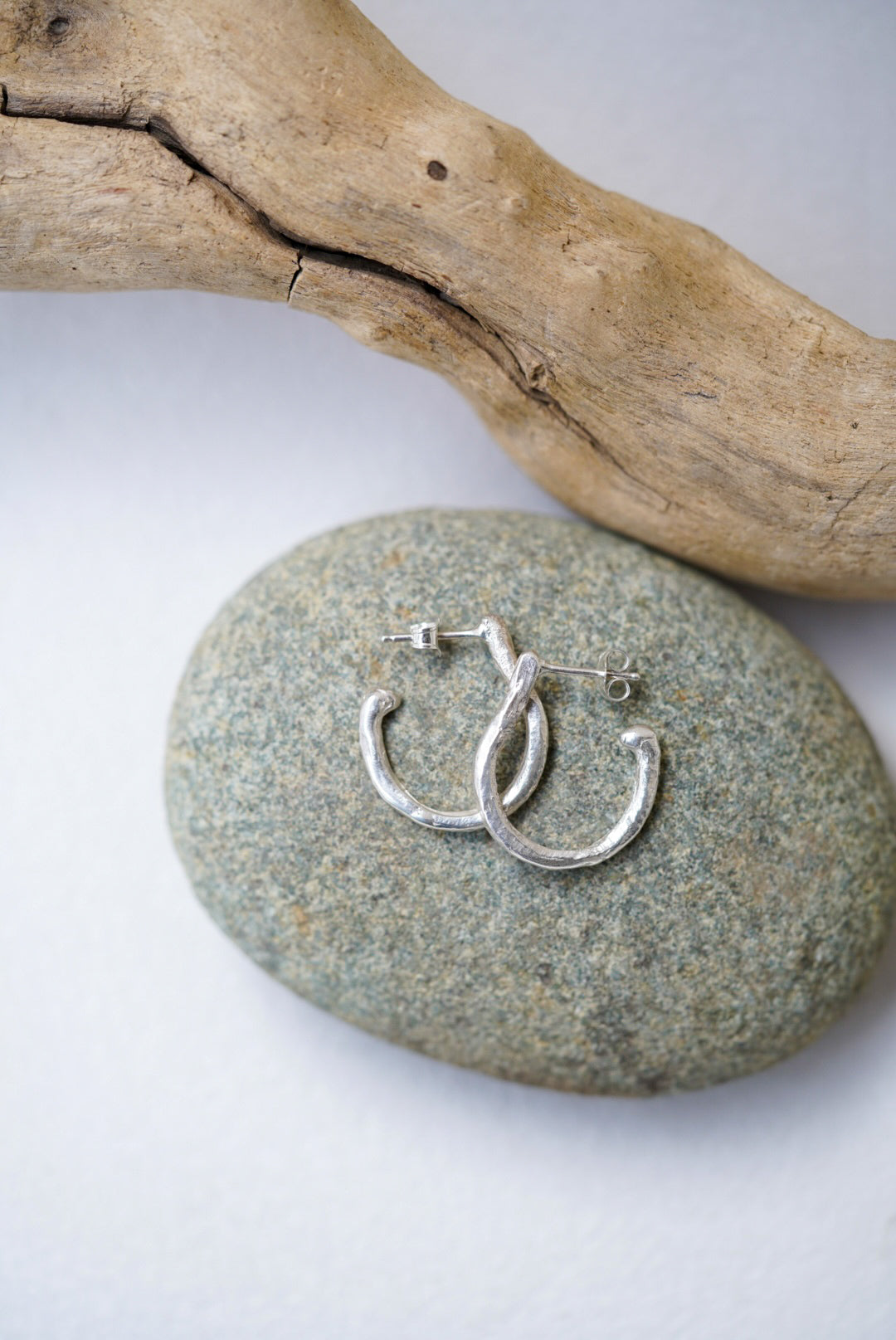 Silver hoop earrings on a stone with a wooden branch in the background