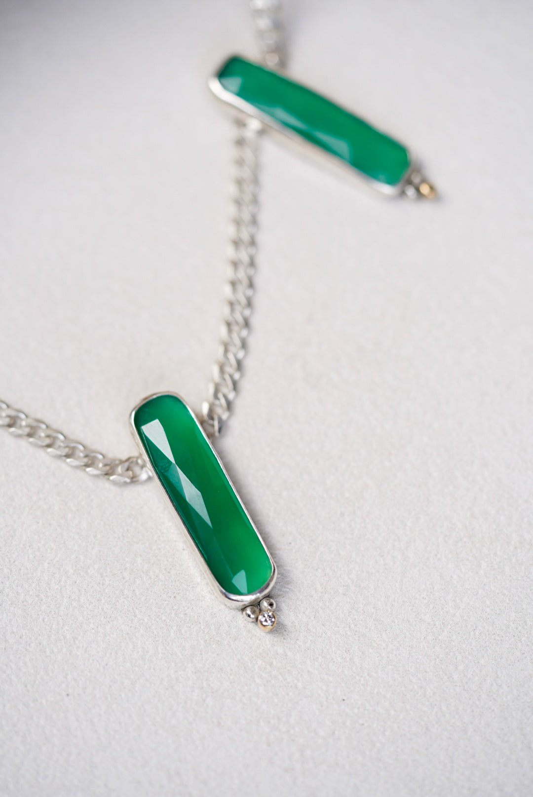 Two green pendant necklaces on a light gray background
