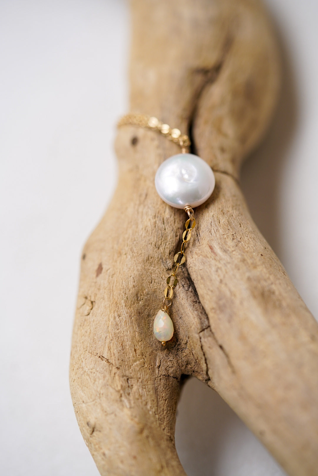 Pearl necklace with gold chain draped over a piece of driftwood on a white background