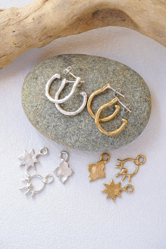 Gold and silver jewelry charms on a stone with a wooden branch in the background