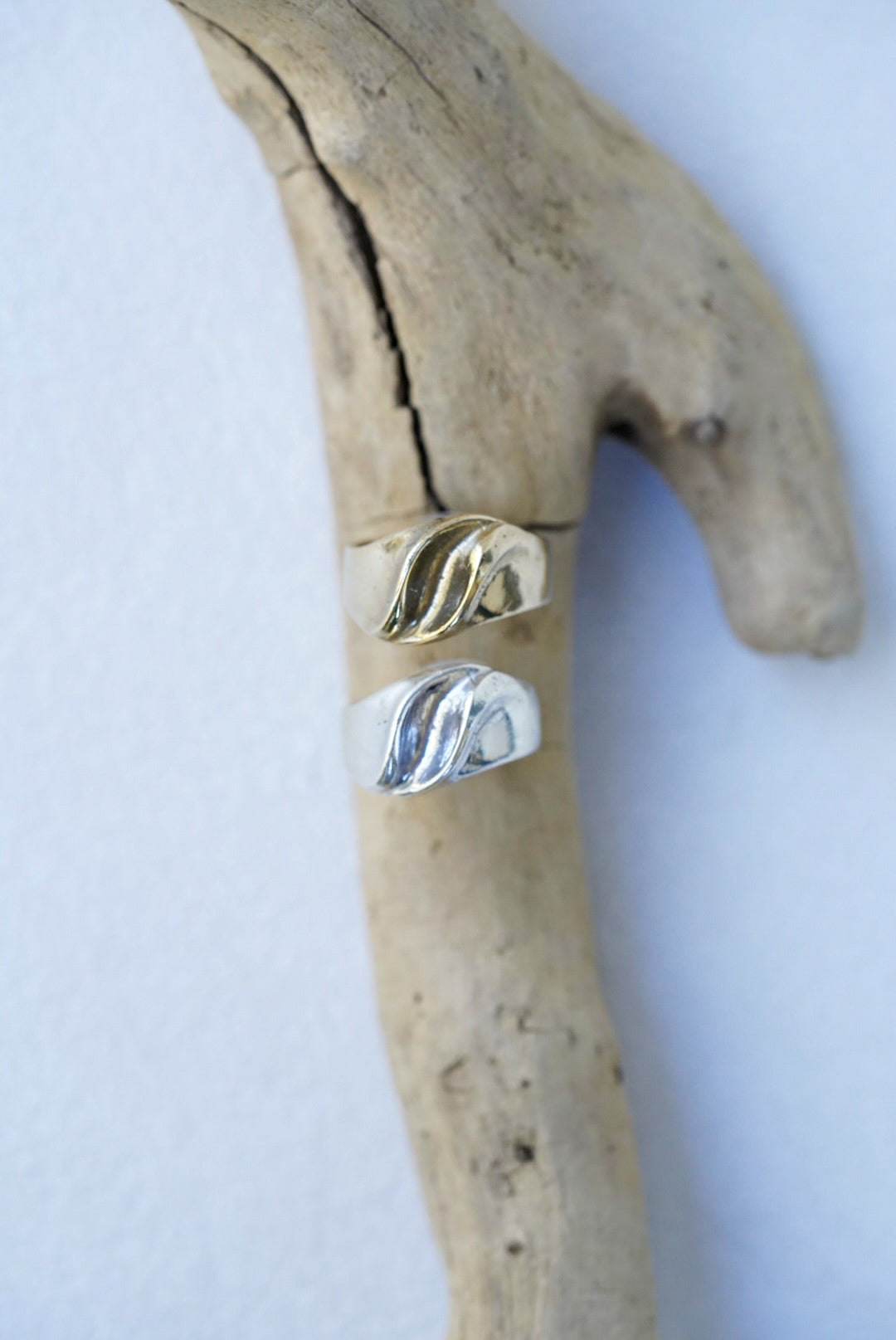 Two rings, one bronze and one silver, on a piece of driftwood against a white background.