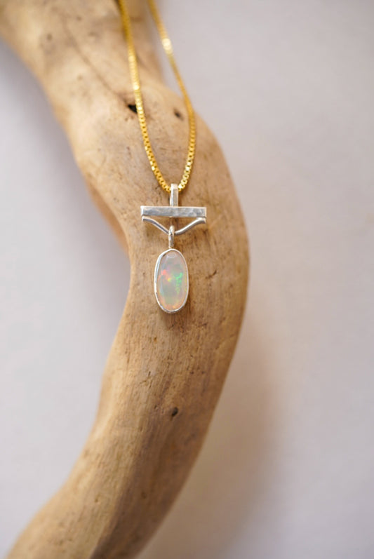 Opal pendant on a gold chain against a wooden background
