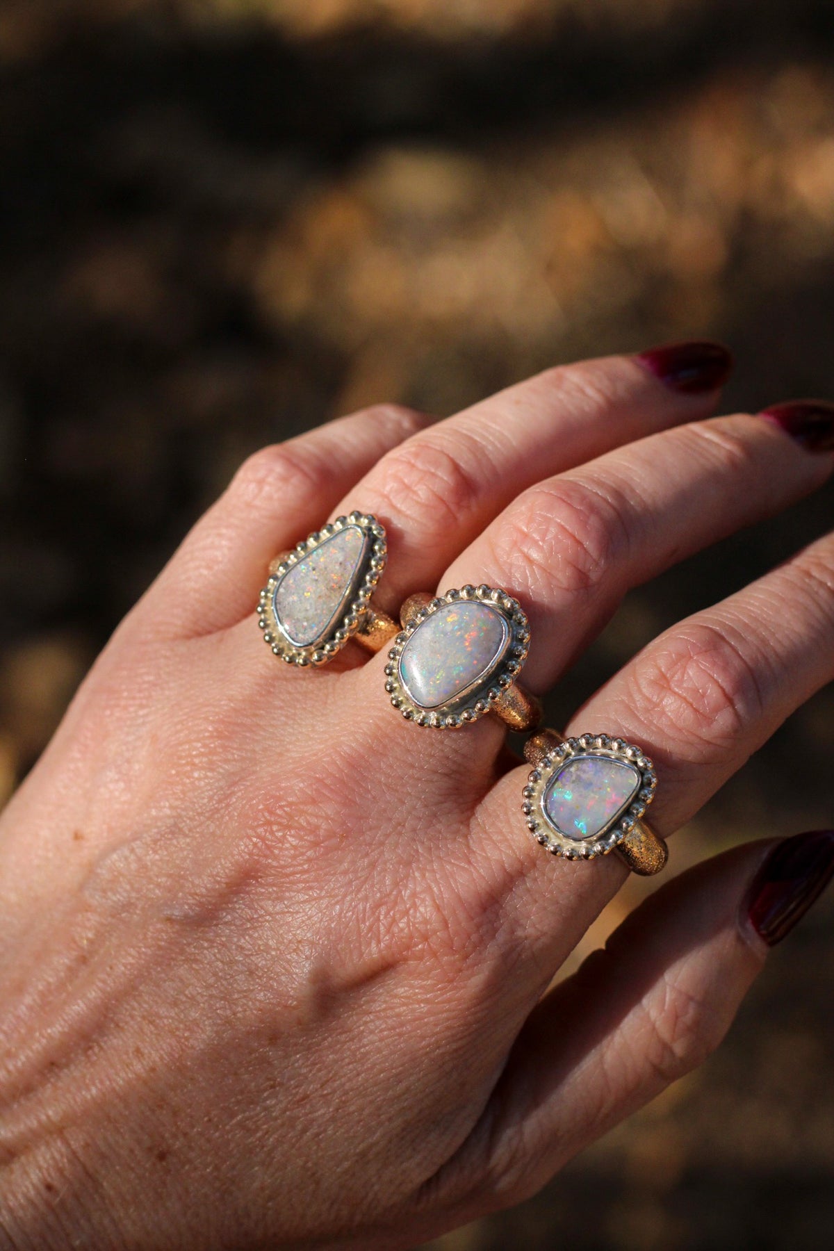 Hand wearing three opal rings with a blurred natural background