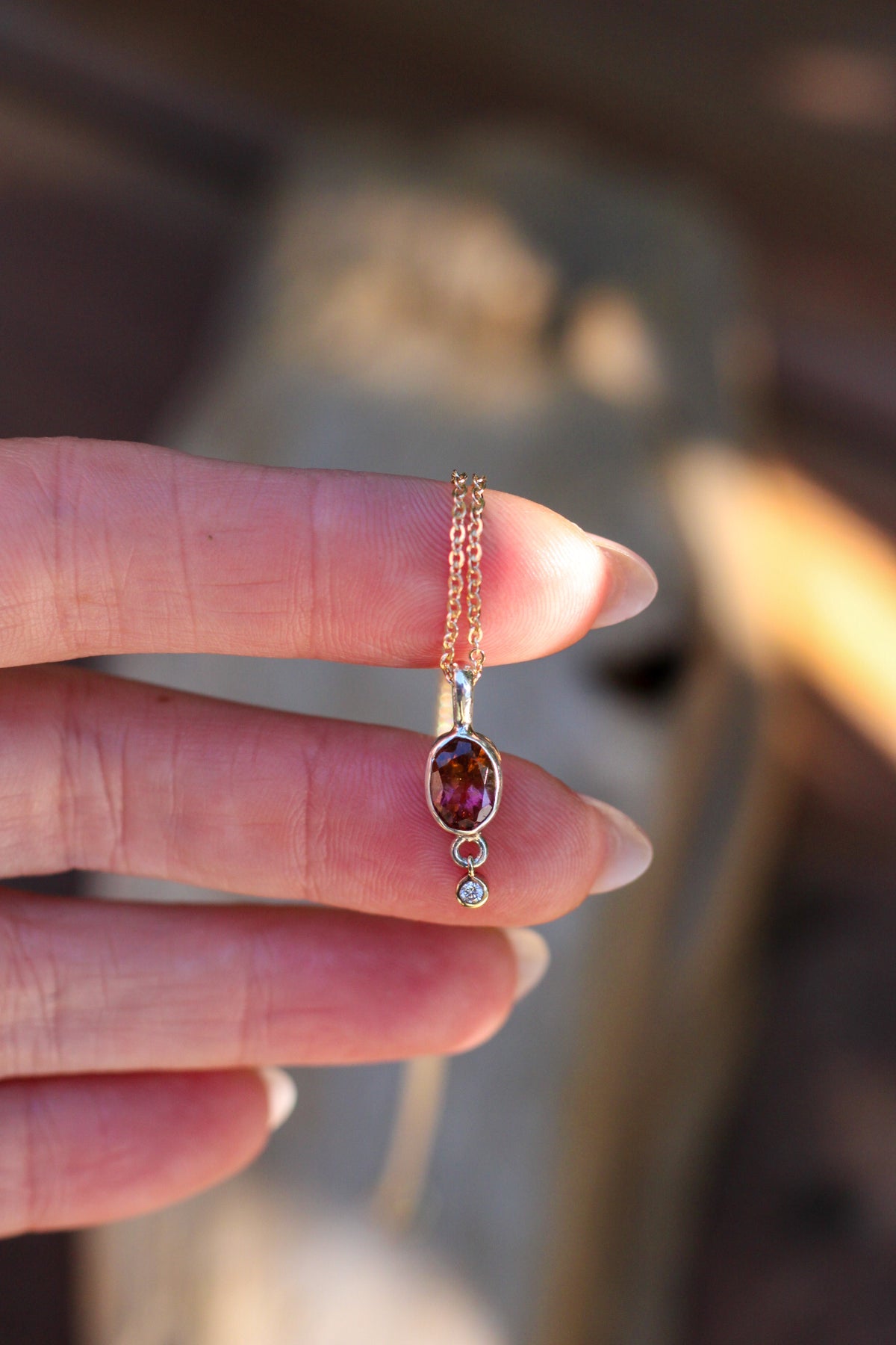 Hand holding a Necklace with a tourmaline and diamond against a blurred background