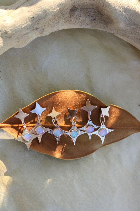 Star-shaped earrings with opals on a leaf-shaped stand against a stone background