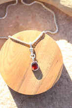 Load image into Gallery viewer, Silver necklace with a red gemstone pendant on a wooden surface