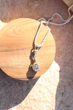 Load image into Gallery viewer, The back of a silver pendant with intricate details with a pendant on a wooden shaped block