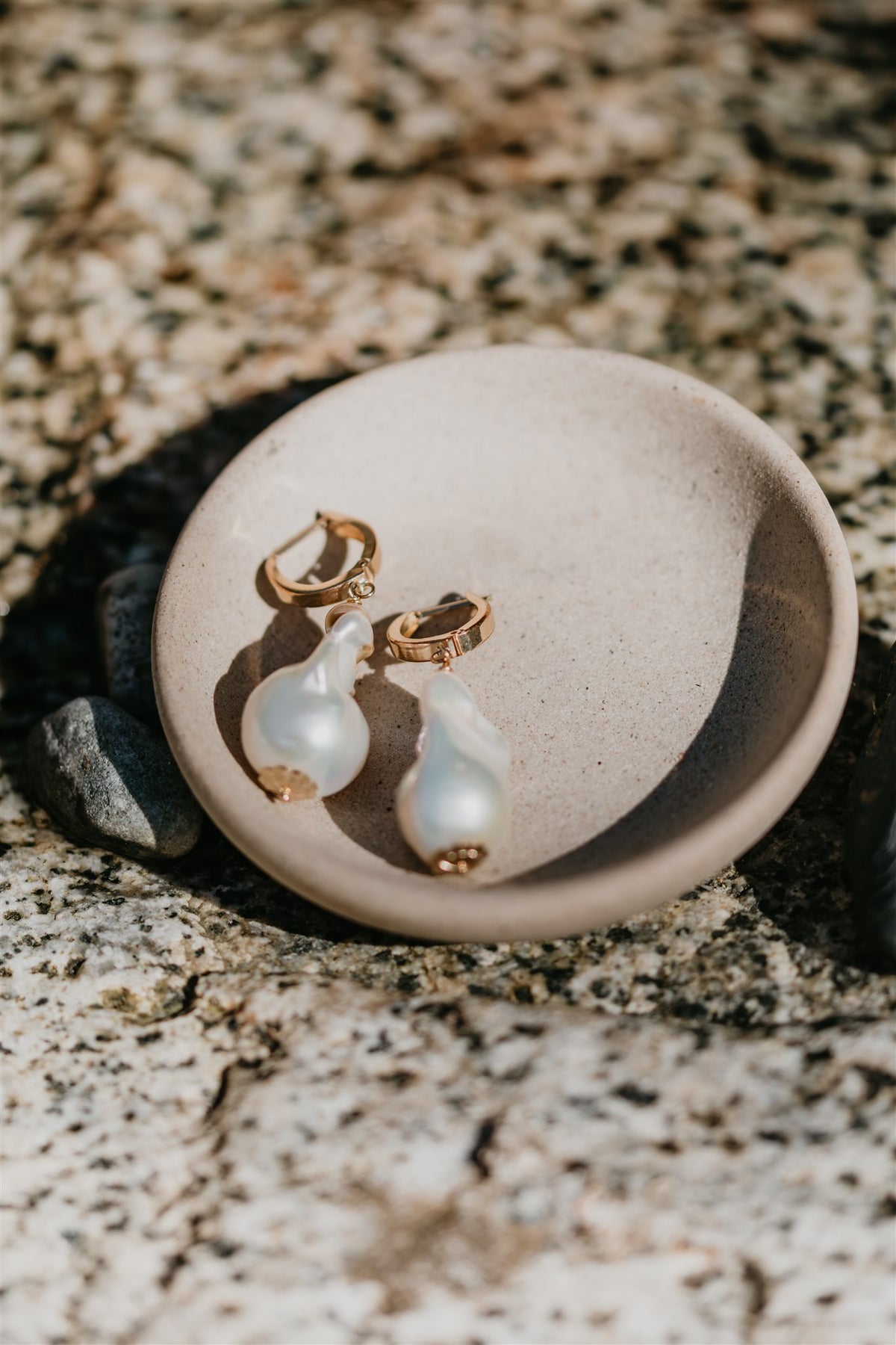 Pearl earrings with gold accents on a white dish against a marble background