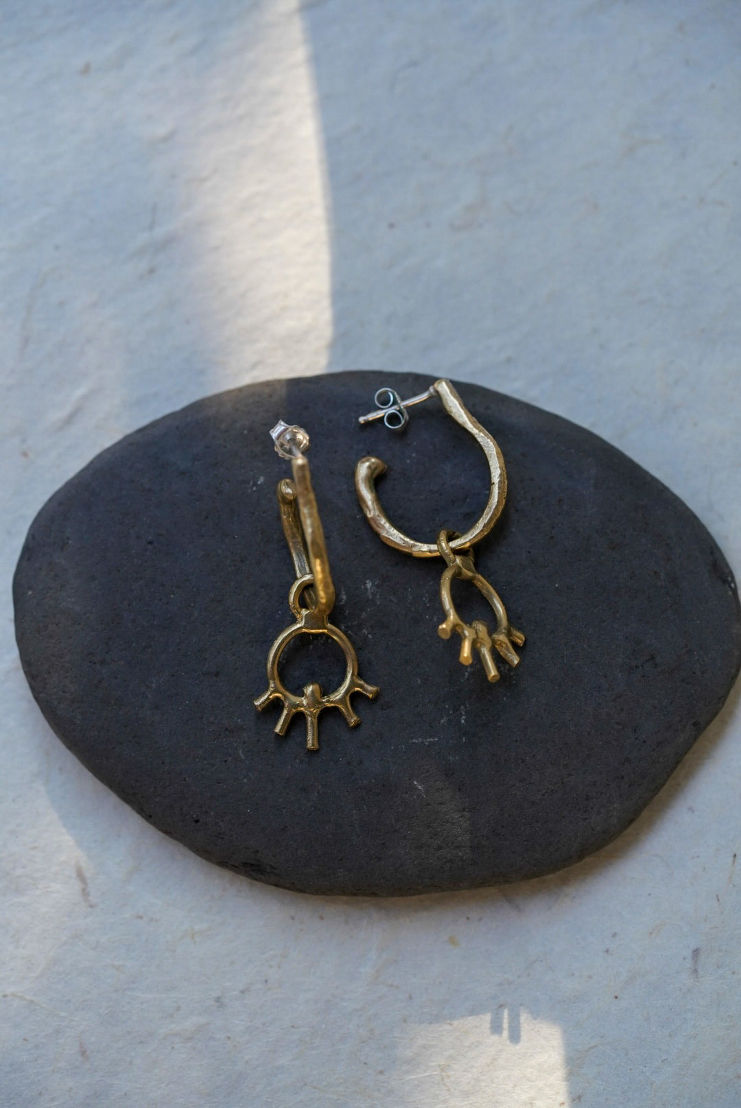 A pair of bronze hoop earrings displayed on a dark oval stone against a light textured background.