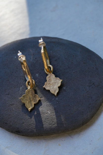 A pair of textured bronze temple charm drop earrings resting on a dark, smooth stone against a light gray background.