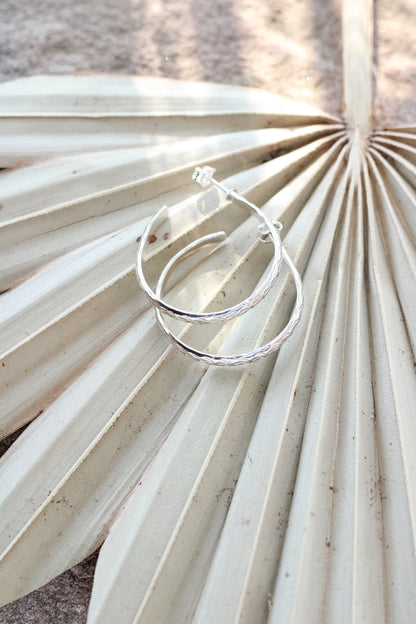 Silver hoop earrings on a palm leaf on a  textured beige surface