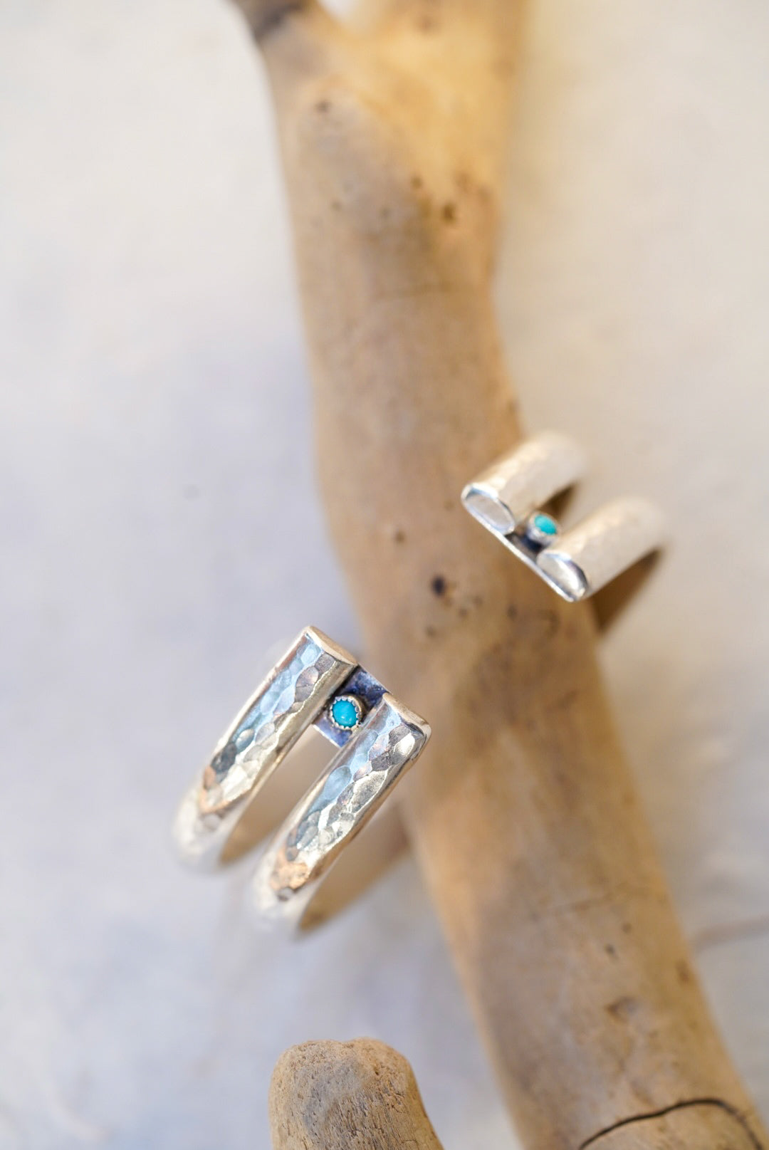 silver split-band cuff with textured hammered edges and a small round turquoise stone, displayed on a natural driftwood branch against a light gray background.