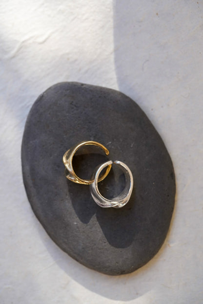Two textured open rings, one bronze and one silver, displayed on a dark gray stone against a light textured background.