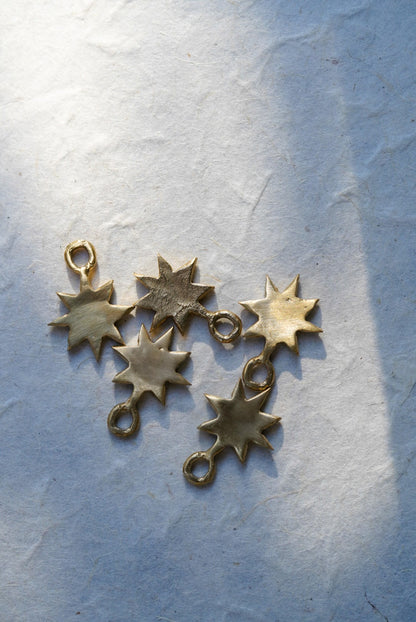 Five bronze star charms with attached loops, arranged on a textured white paper background with soft shadows.