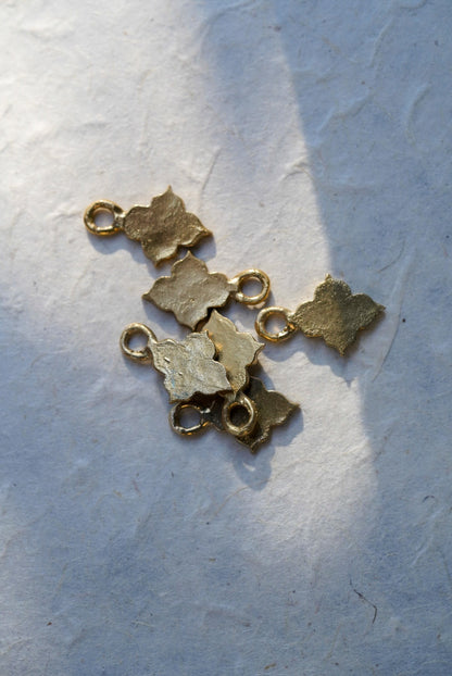 Five small textured bronze temple-shaped charms arranged on a light gray textured paper background