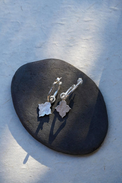A pair of silver hoop earrings with dangling temple shaped charms, displayed on a dark stone against a textured light gray background.