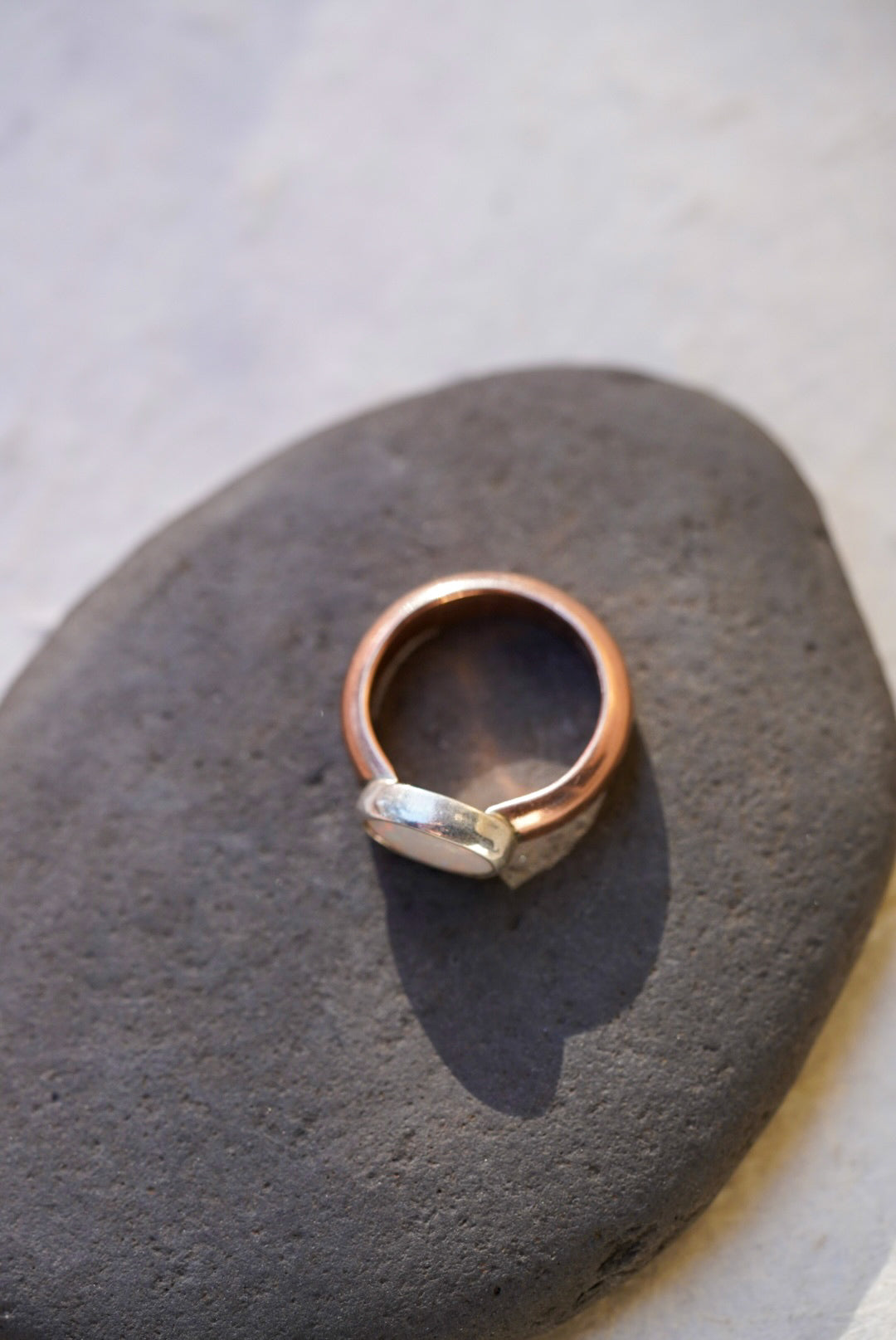 A handmade ring with a rose gold band and a opal set in a bezel, resting on a dark gray stone.