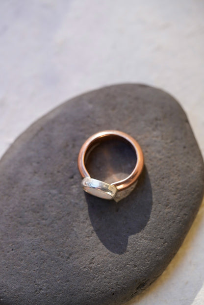 A handmade ring with a rose gold band and a opal set in a bezel, resting on a dark gray stone.
