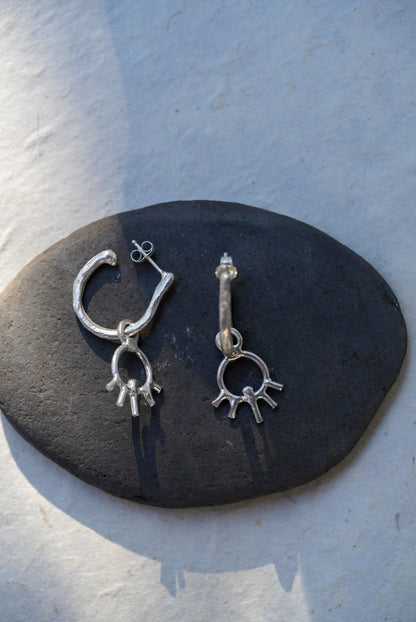 A pair of silver dangle earrings displayed on a dark oval stone against a light textured background.