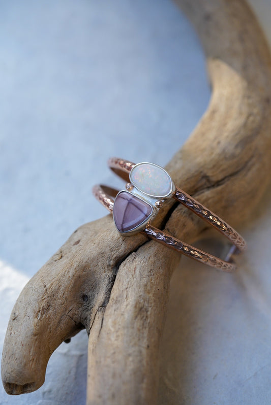 A textured rose gold double band cuff with an opal and jasper, displayed on a piece of driftwood.
