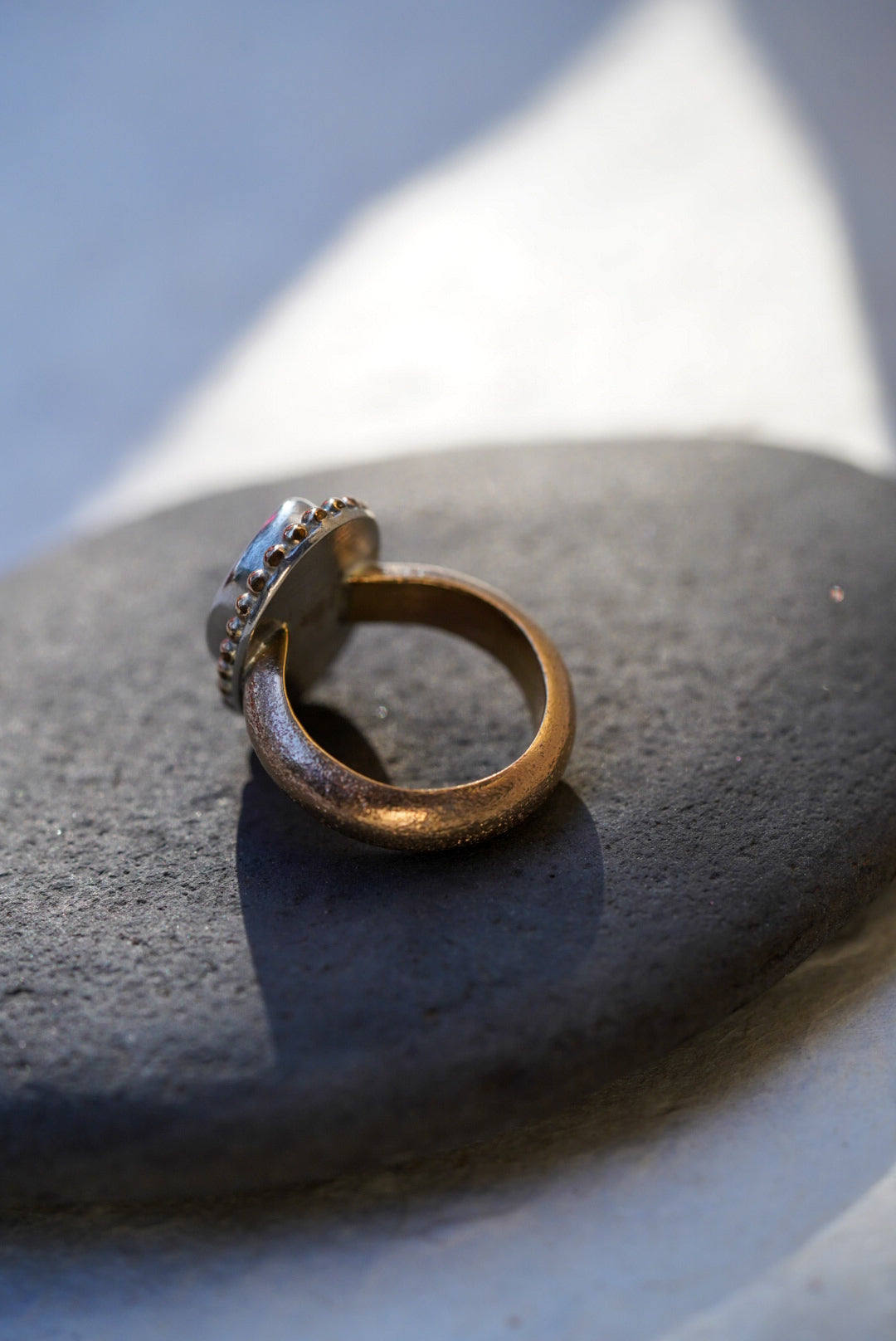 A textured gold ring with a sparkly band, resting on a smooth dark gray stone under natural light.
