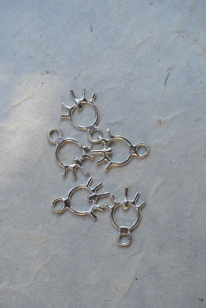 Five silver sun charms, arranged on a textured off-white surface.