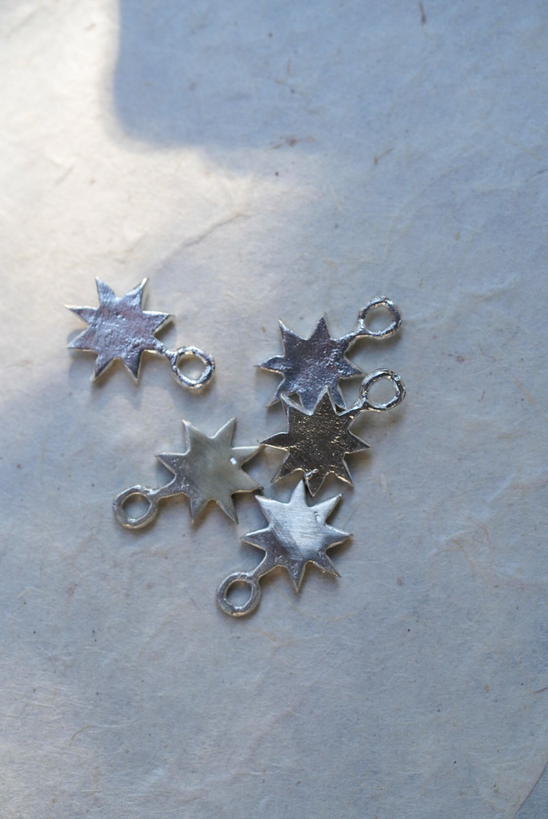 Five silver star charms arranged on a textured off-white paper background.