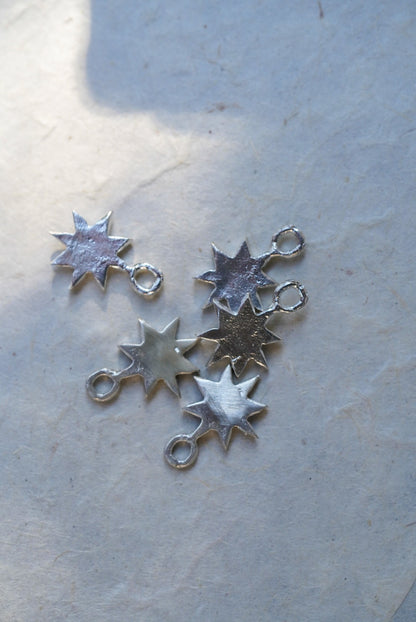Five silver star charms arranged on a textured off-white paper background.