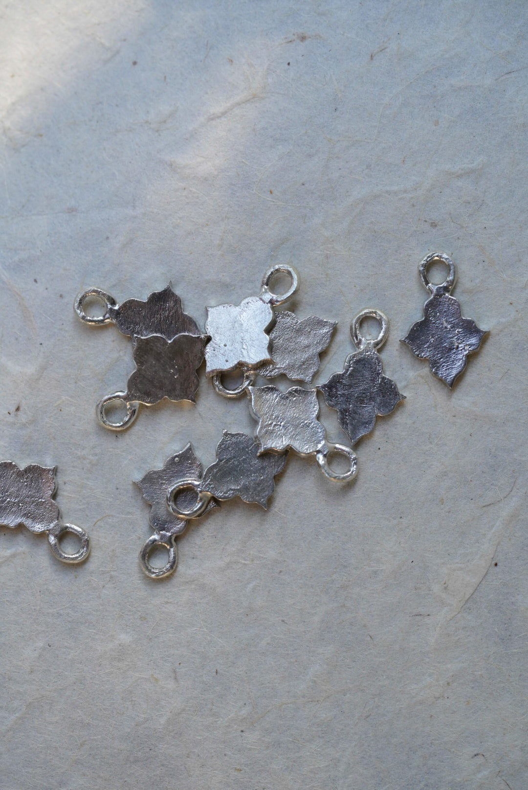 Several small textured silver charms with loop tops scattered on a light gray surface.