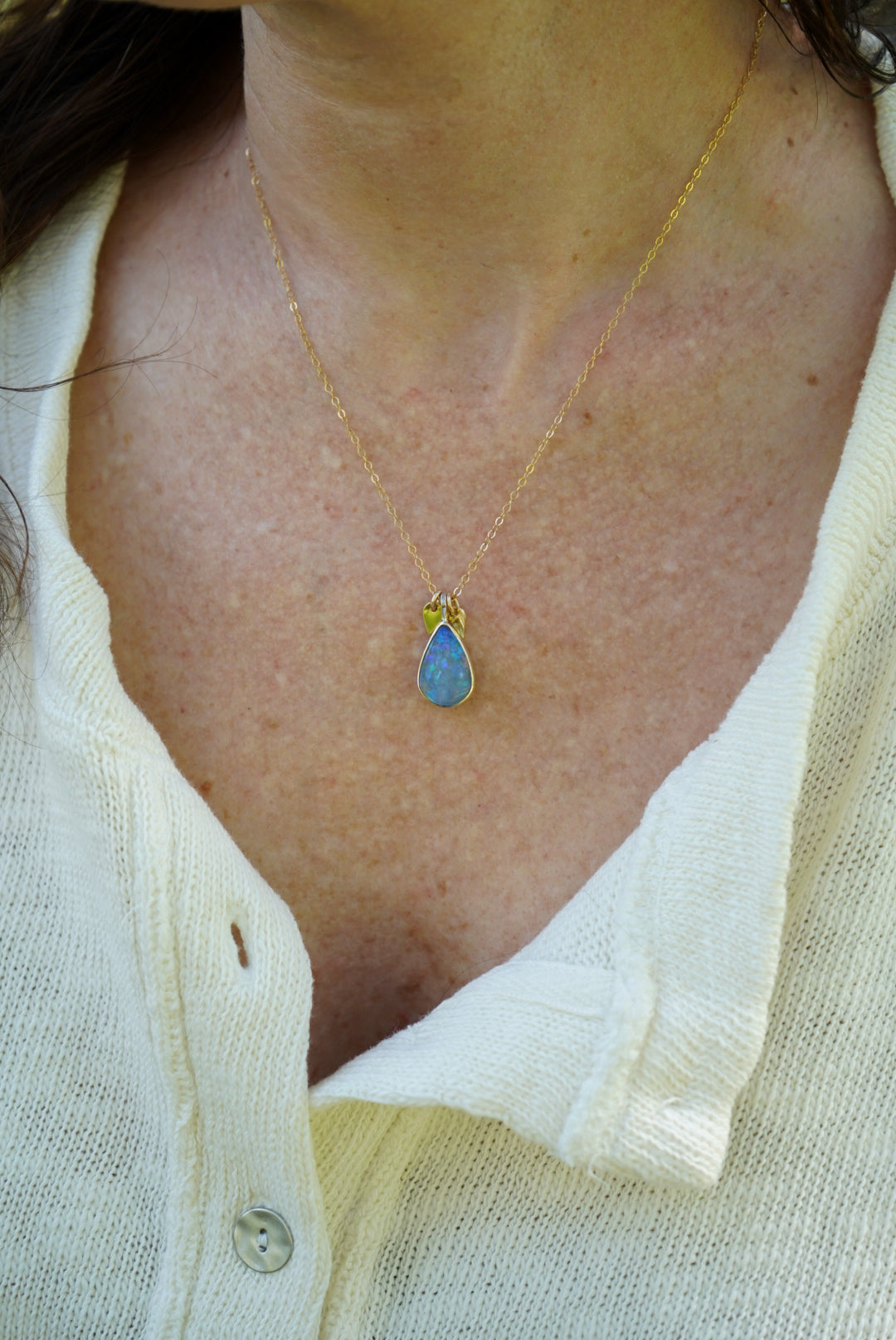 Close-up of a necklace with a blue pendant worn by a person in a light-colored shirt.