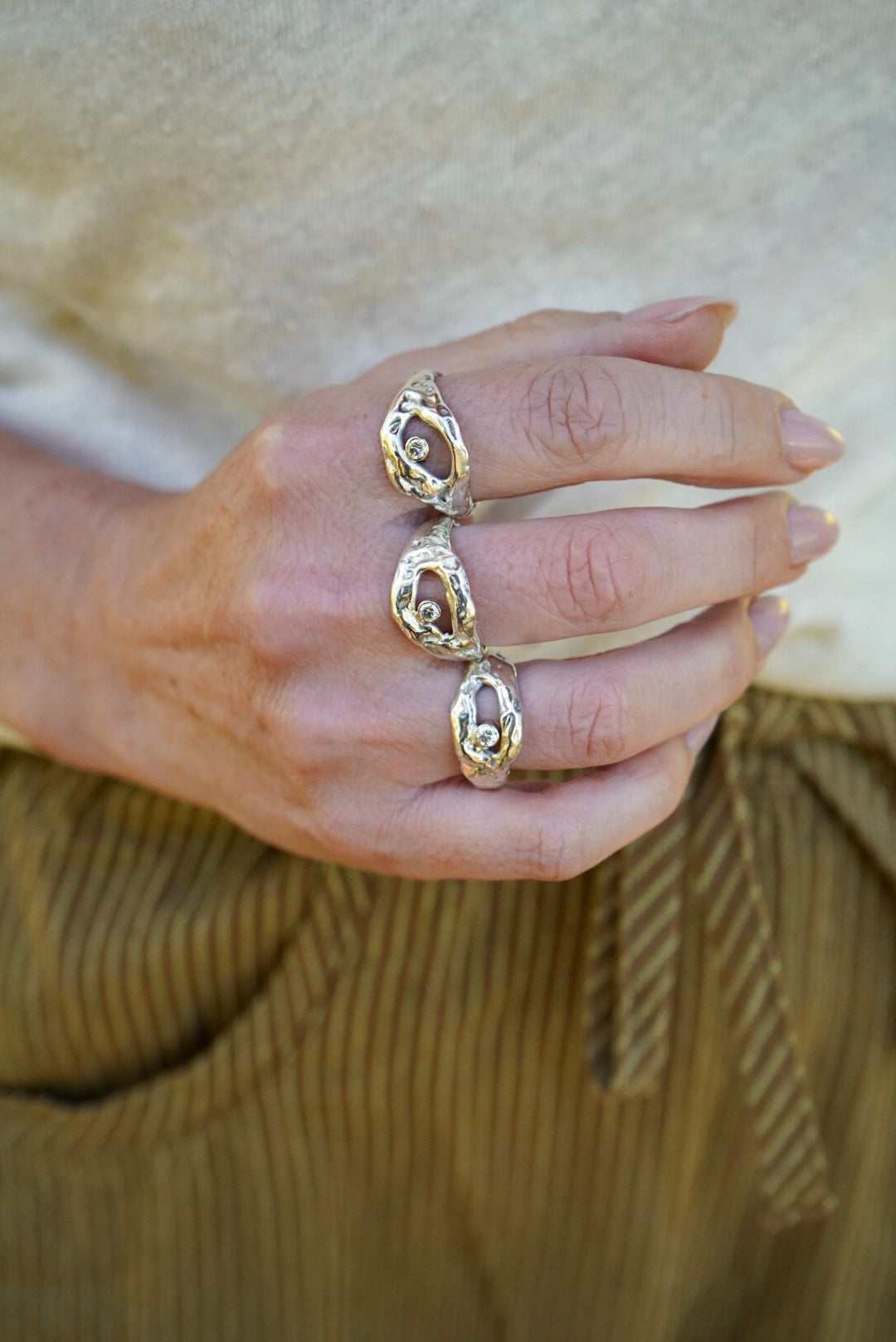 Close-up of a hand wearing silver rings with a beige background