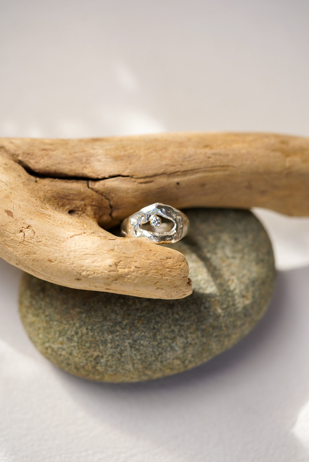 Silver ring with a diamond on a stone next to a piece of driftwood