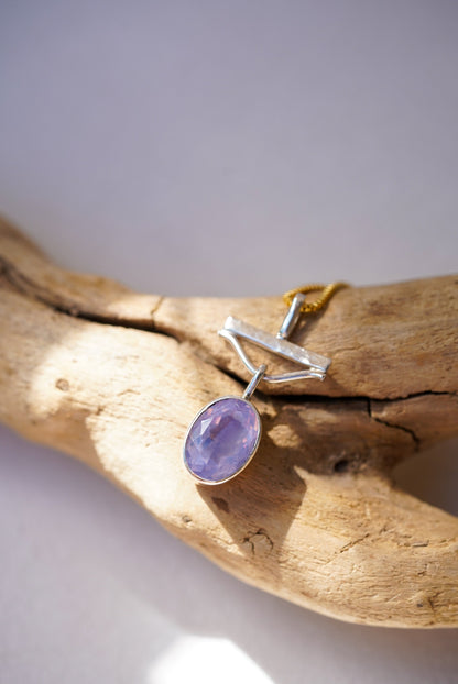 Jewelry with a purple gemstone on a piece of driftwood against a light background