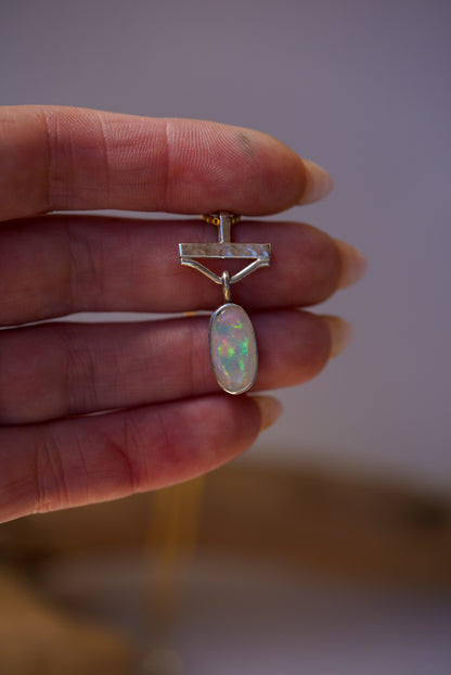 Opal pendant held between fingers against a neutral background