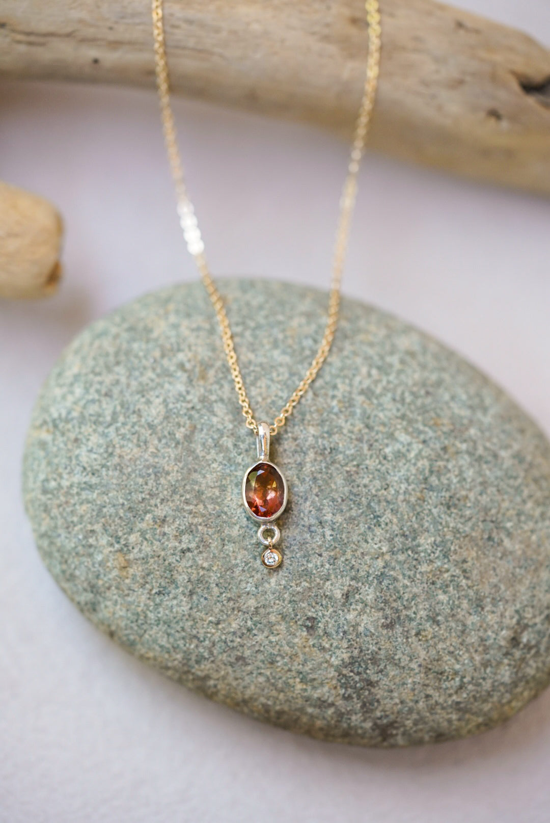Tourmaline pendant necklace with a diamond dangling underneath, on top of a river rock