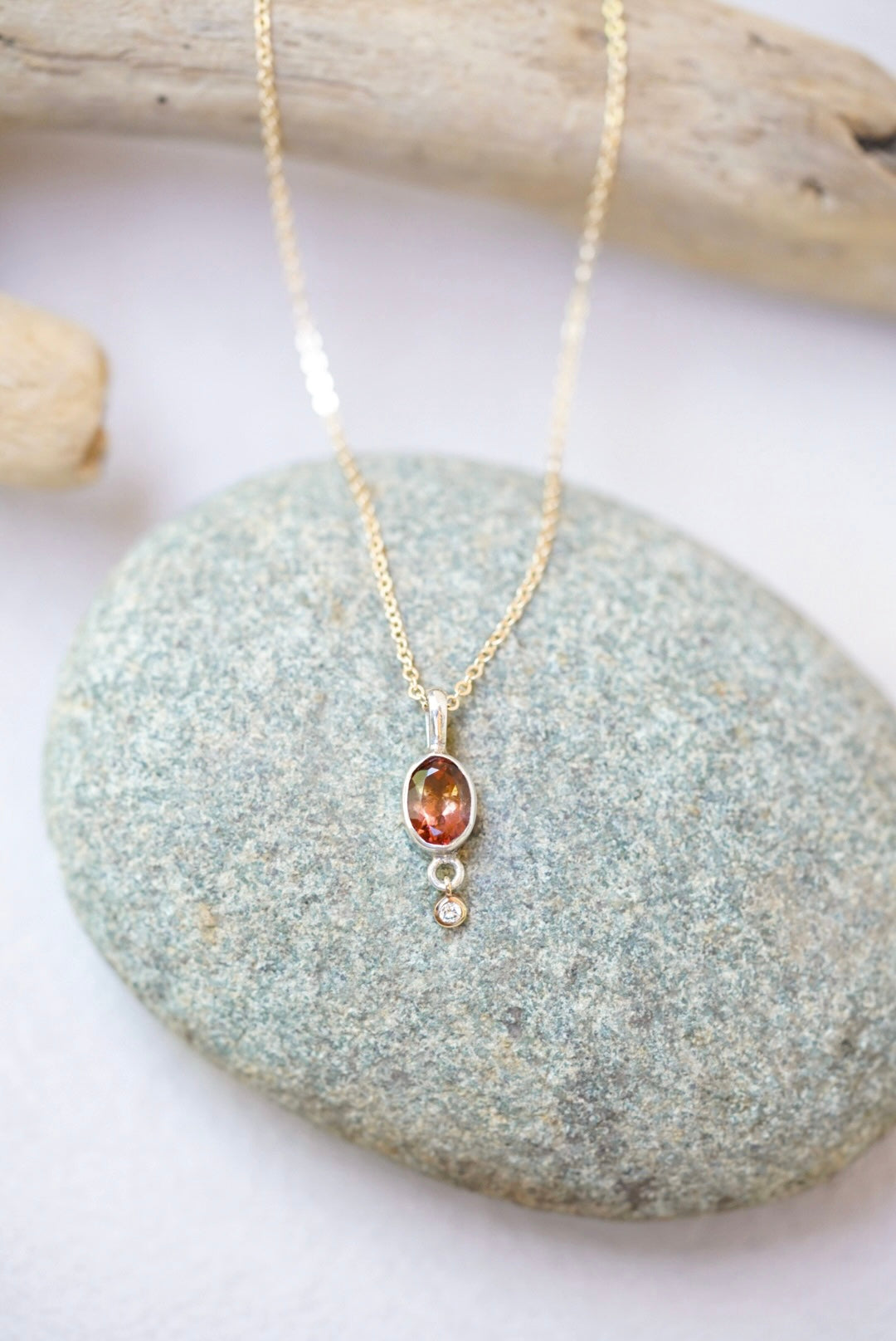 Tourmaline pendant necklace with a diamond dangling underneath, on top of a river rock