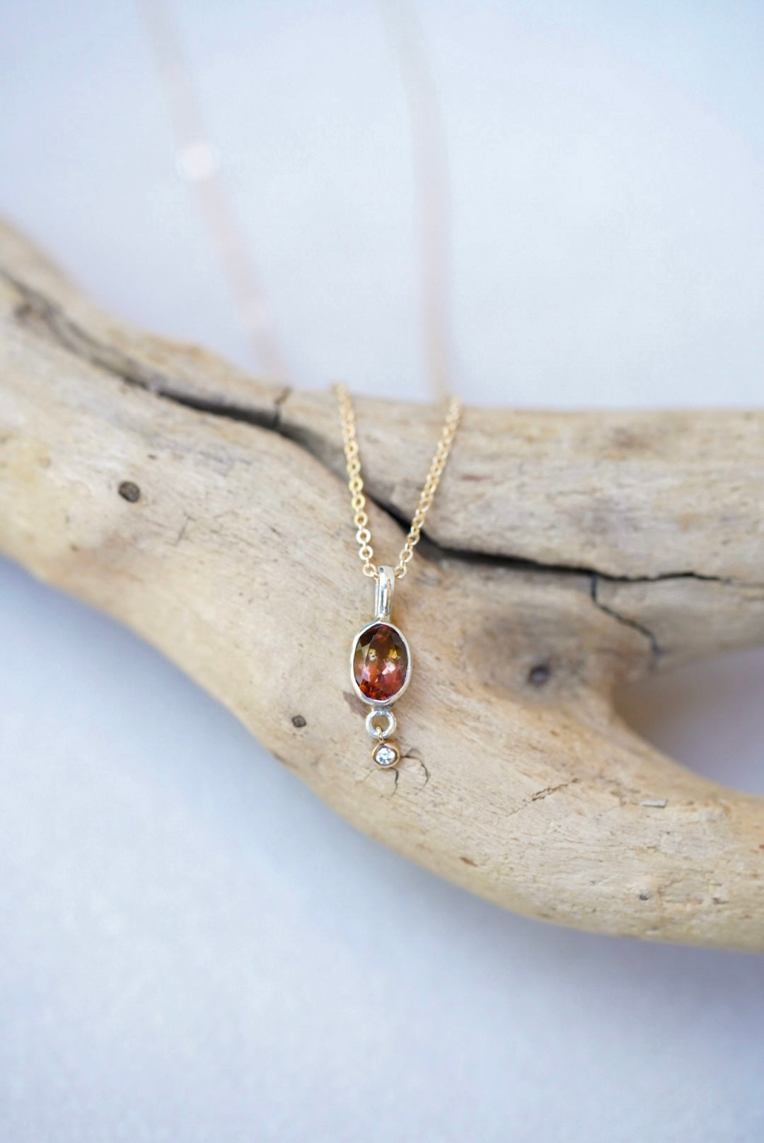 Tourmaline pendant necklace with a diamond dangling underneath, on top of a piece of driftwood