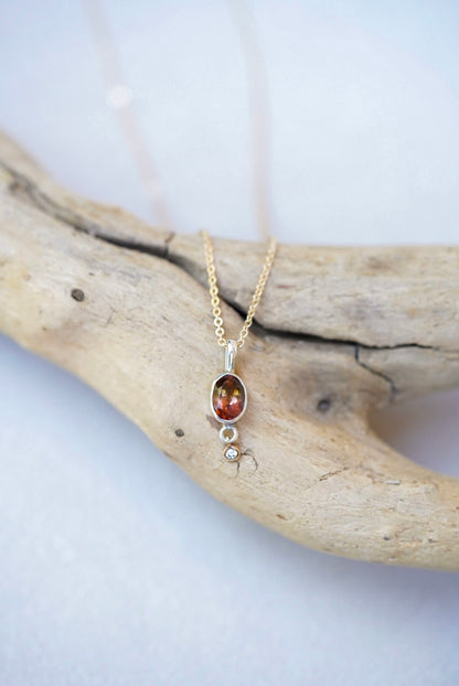Tourmaline pendant necklace with a diamond dangling underneath, on top of a piece of driftwood