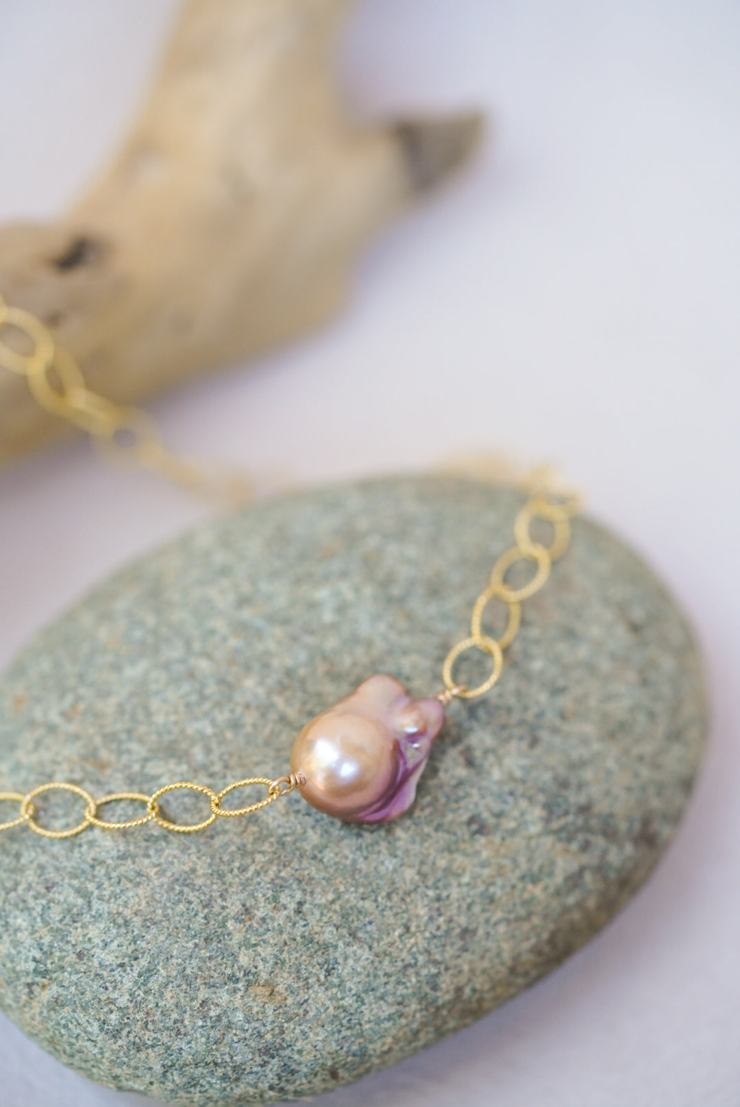 Gold chain necklace with a pink pearl on a stone surface