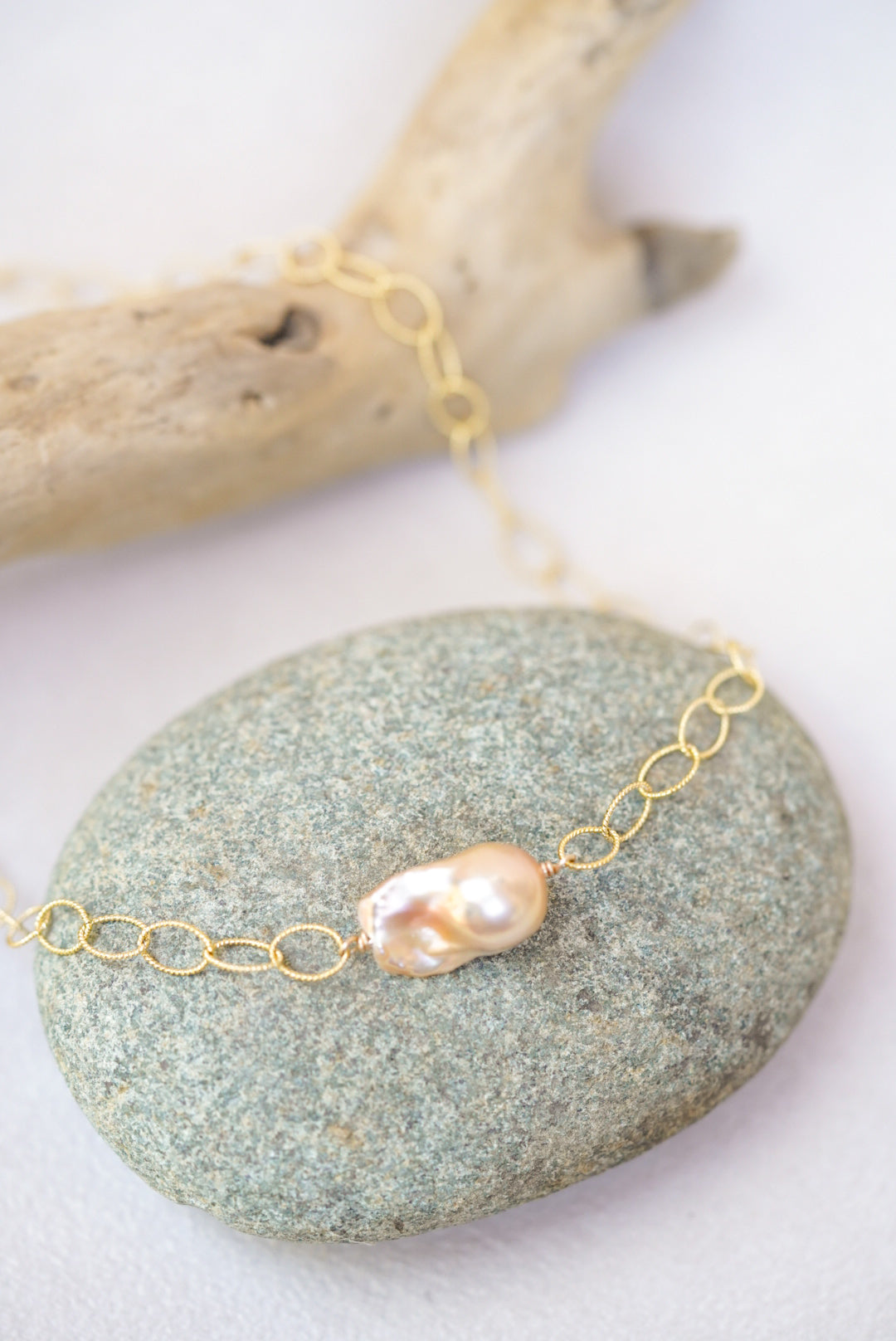 Gold chain necklace with a pearl on a stone surface