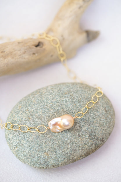 Gold chain necklace with a pearl on a stone surface