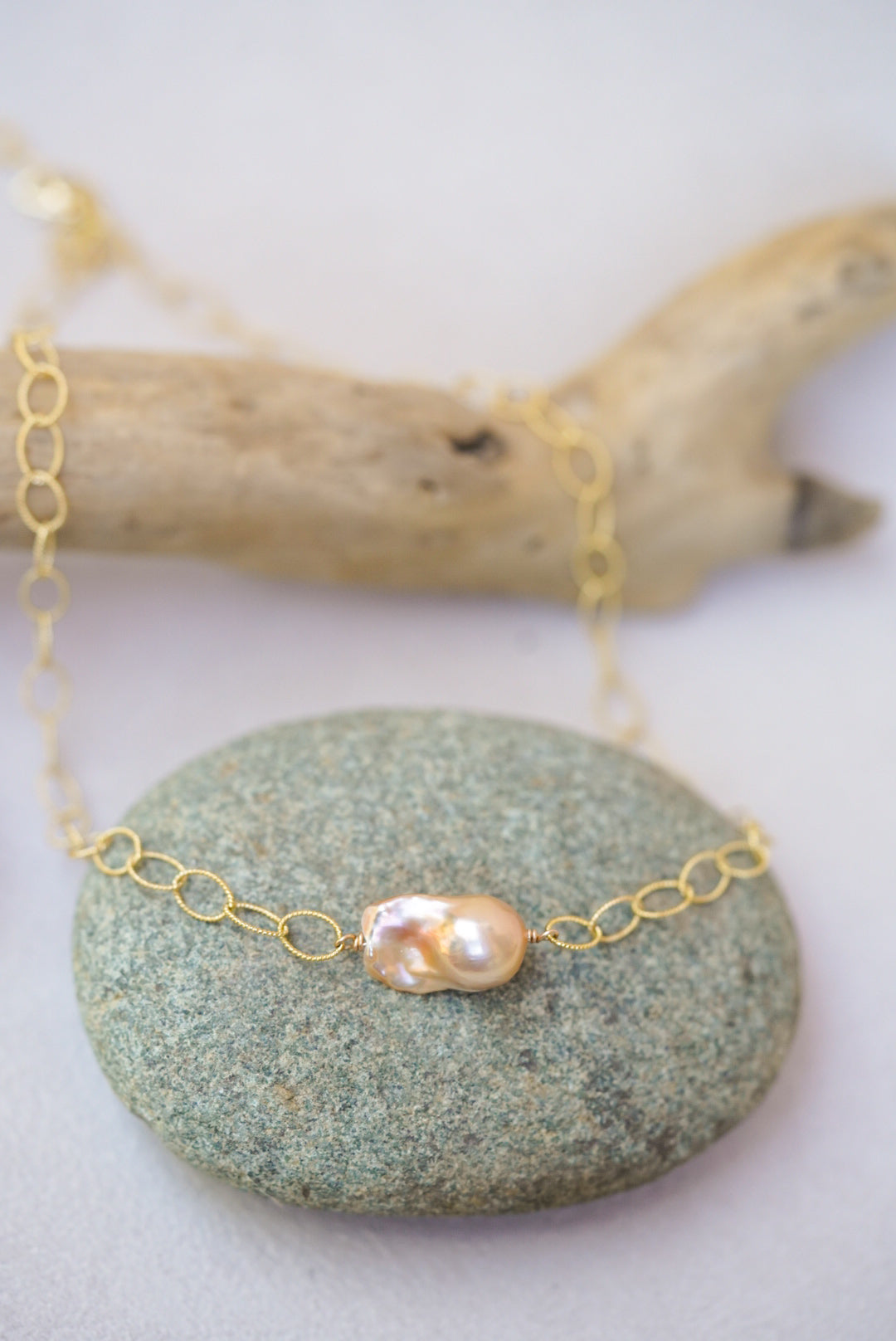 Gold necklace with a pearl pendant on a stone surface