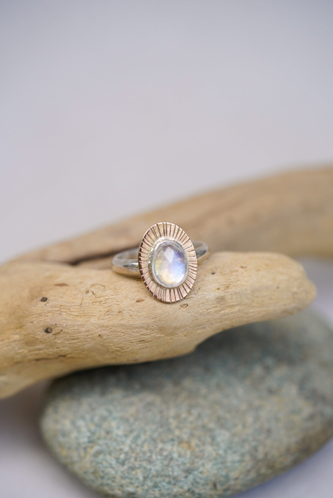 Moonstone ring on top of a piece of driftwood with a white background