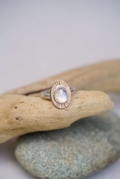 Moonstone ring on top of a piece of driftwood with a white background