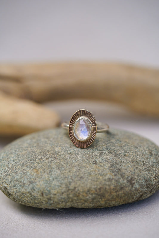 Moonstone ring on top of a rock with driftwood and a white background